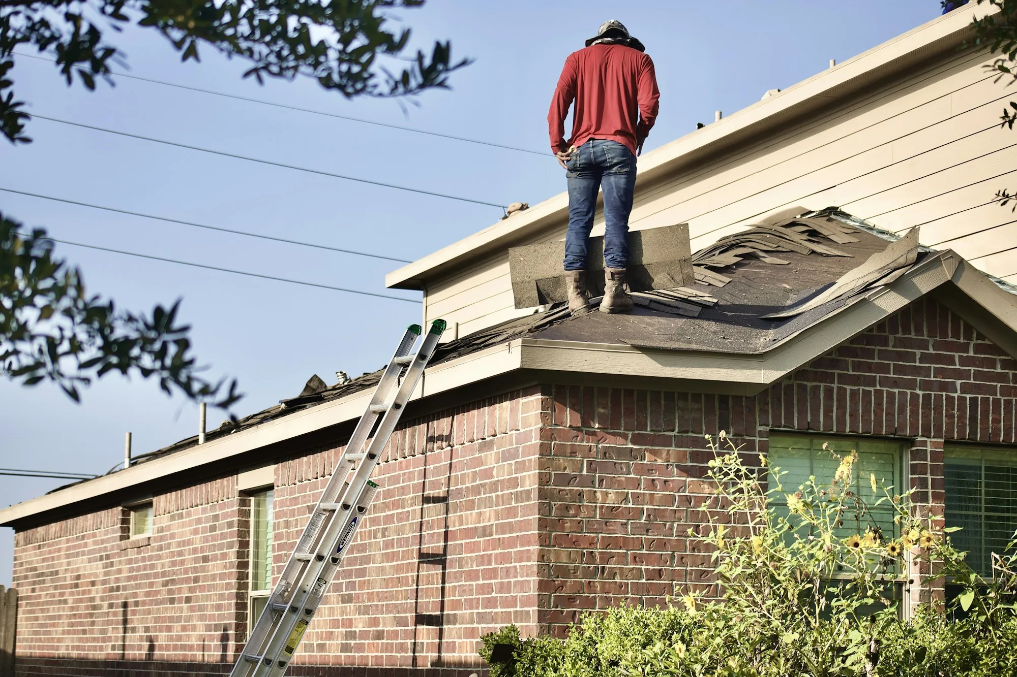 A roofer at the ridge of a shingle roof